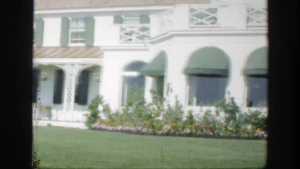 1950 Montreal 8mm view of a white building with green awnings, shutters, flower beds, and trimmed grass.