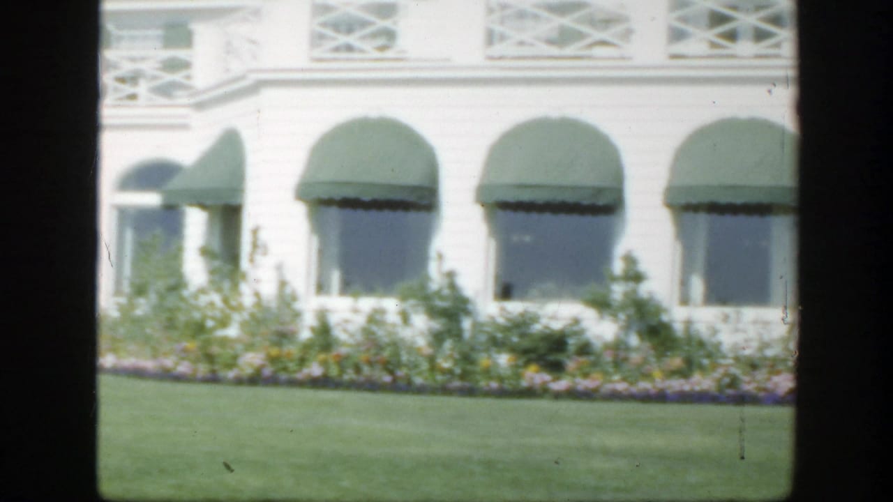 1950 Montreal exterior showing green window awnings on a white facade above a planted garden and lawn.