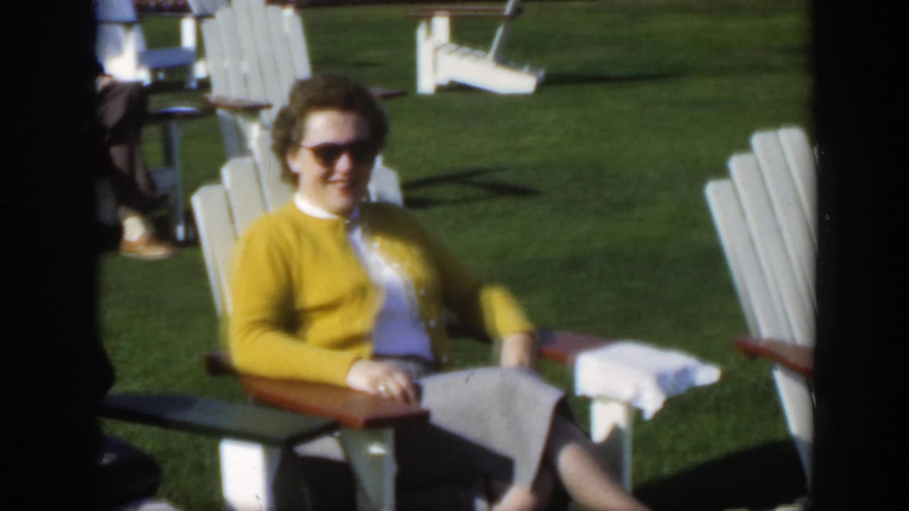 1950 Montreal frame showing an older woman in sunglasses seated on a white Adirondack chair, with lawn chairs in the background.