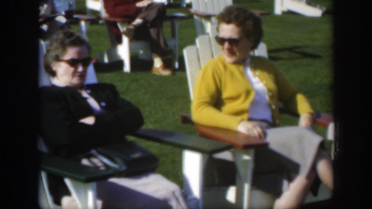 In 1950 Montreal home-movie footage, two women in sunglasses relax in white lawn chairs on a sunny green lawn.