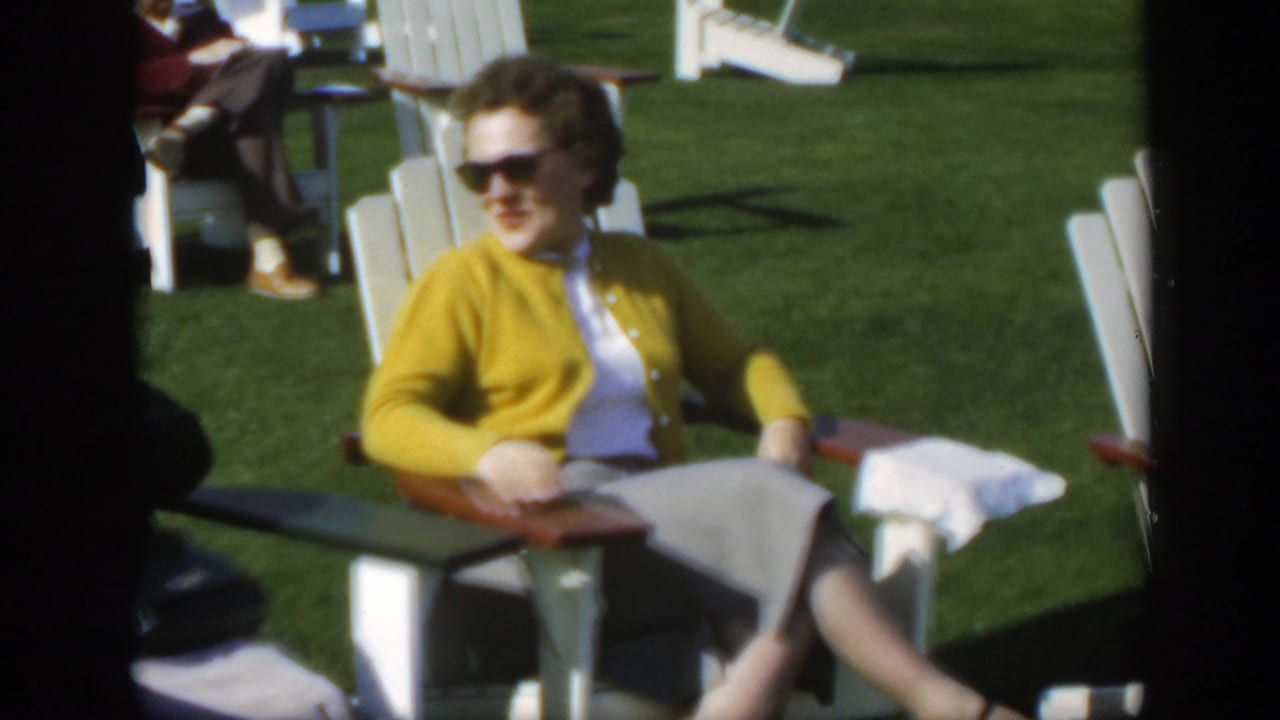 Woman in a yellow cardigan sits in a white lawn chair on grass.