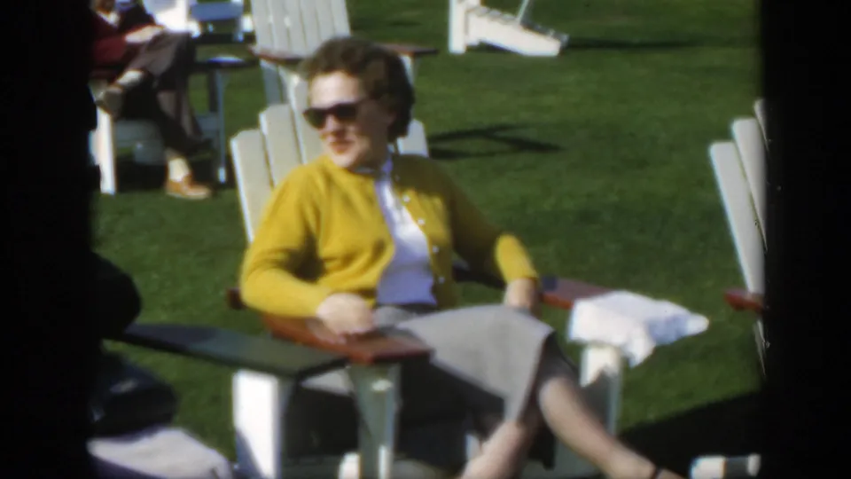 A woman in a yellow cardigan and sunglasses sits in a white Adirondack-style chair on a Montreal lawn in 1950 footage.