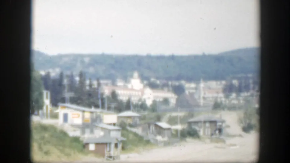 1950 Montreal home-movie frame with a distant view of buildings, trees, and hills, softened by 8mm exposure and framing.
