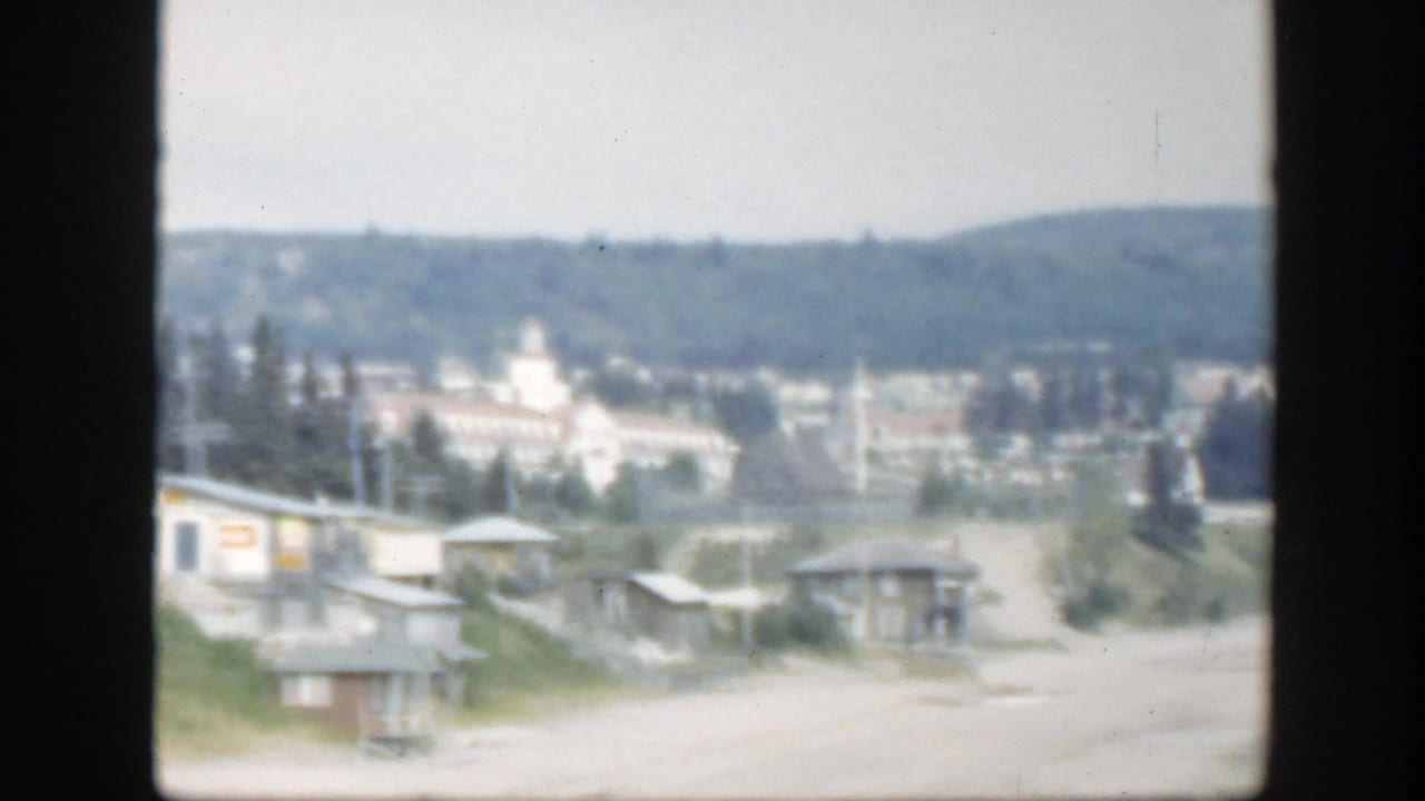 Soft distant view of beachside houses, trees, hills, and a pale towered building.