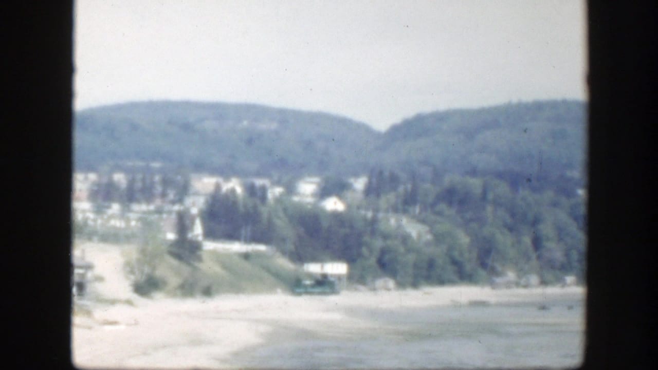Soft 8mm view of hillside houses and trees beyond a pale open area.