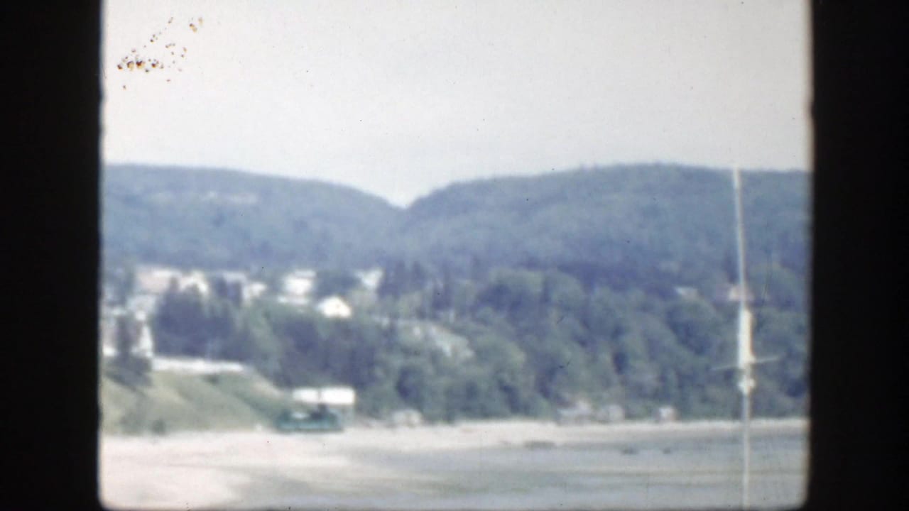 Soft 1950 Montreal view of wooded hillside, scattered houses, and a pale open area, with visible 8mm frame borders.