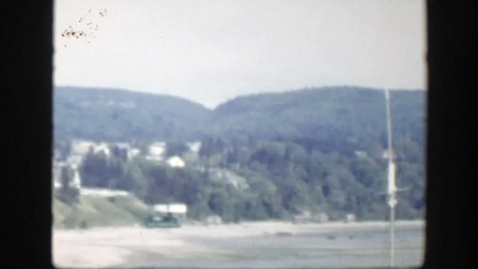 Soft 1950 Montreal view of wooded hillside, scattered houses, and a pale open area, with visible 8mm frame borders.
