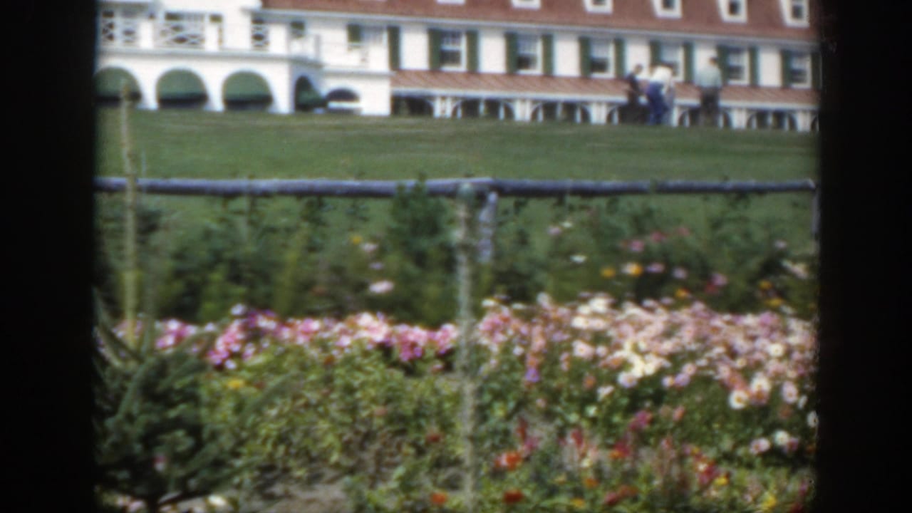 1950 Montreal 8mm frame showing pink and white flowers, a wooden fence, green lawn, and a white building with red roof dormers.