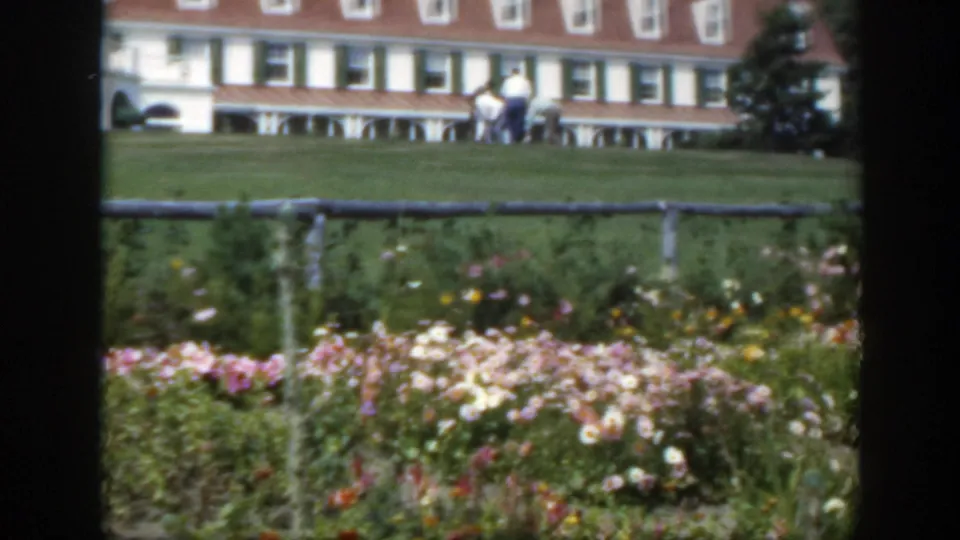 1950 Montreal garden view with flowers in front, several men on the lawn, and a white building with green shutters behind them.