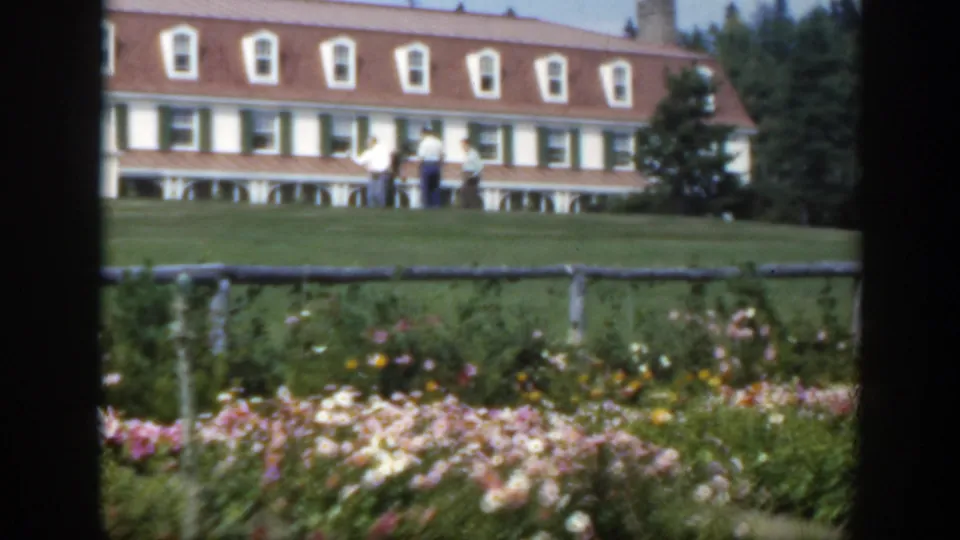 1950 Montreal 8mm frame of a landscaped garden with men on the grass in front of a white building with a red roof.