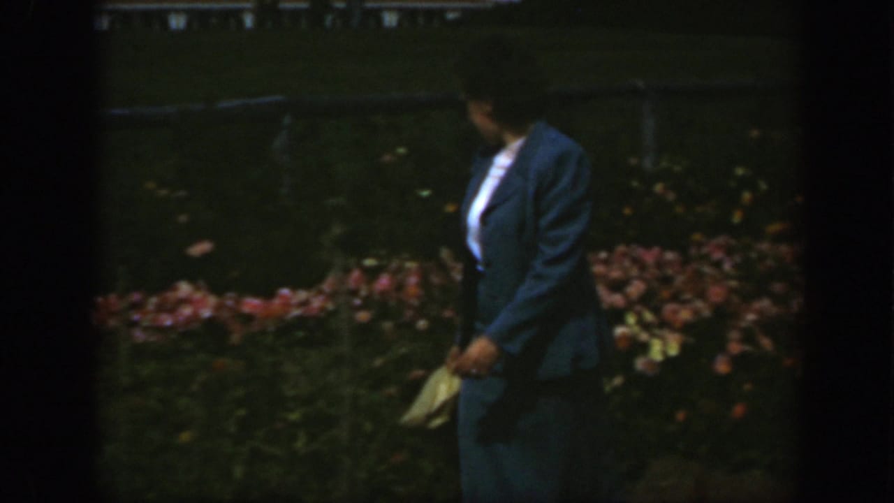The woman turns slightly in a Montreal garden, with flowers and a low fence or railing behind her.