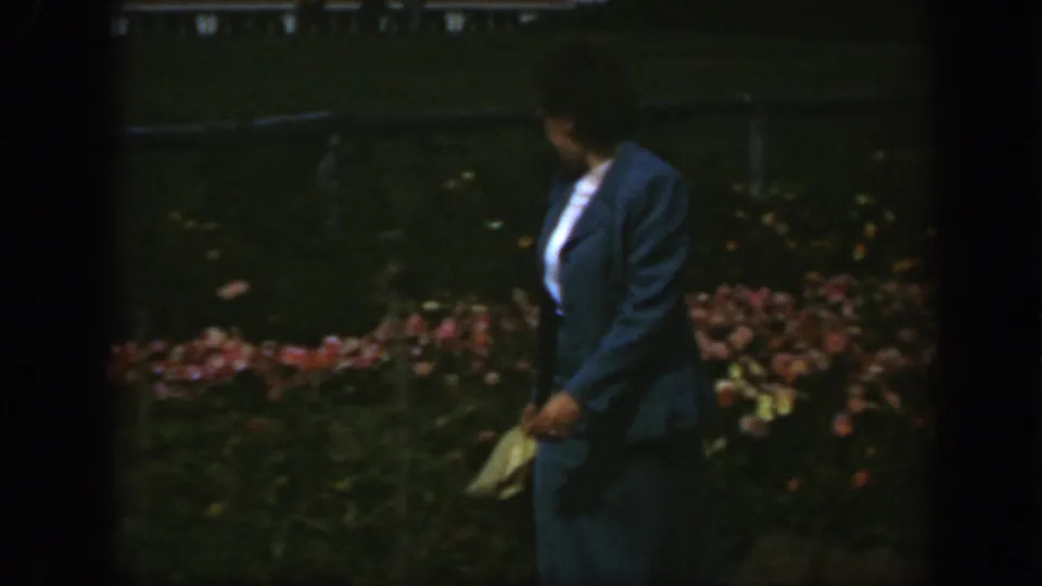 The woman turns slightly in a Montreal garden, with flowers and a low fence or railing behind her.