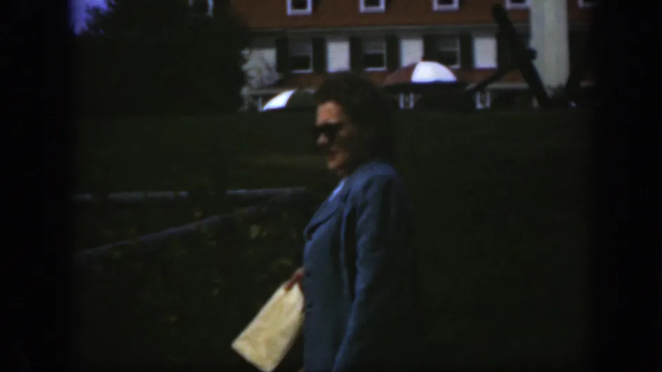 The woman appears to smile toward the camera while holding a light-colored bag on the Montreal lawn.