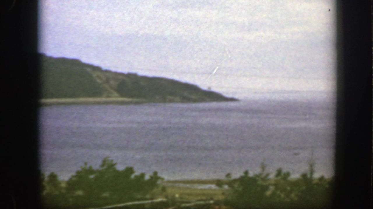 1950 8mm frame near Montreal with a green headland, broad water surface, low shoreline, and soft overcast light.