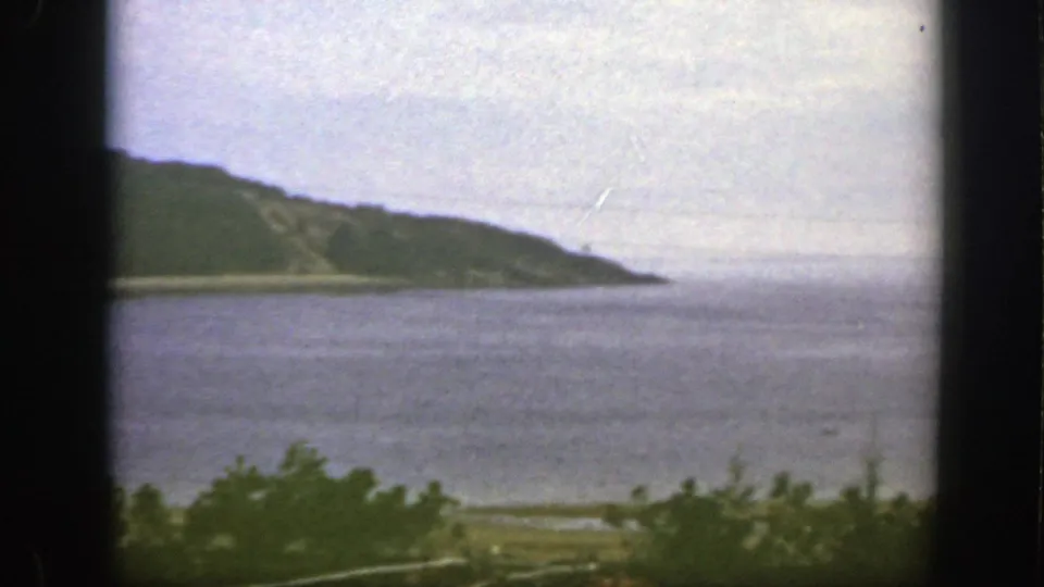 1950 8mm frame near Montreal with a green headland, broad water surface, low shoreline, and soft overcast light.