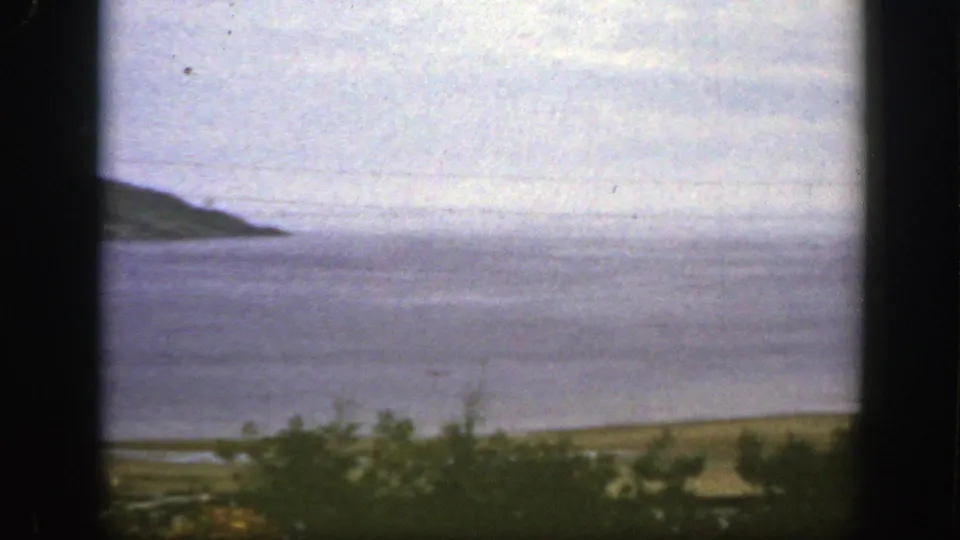1950 8mm home-movie frame near Montreal showing open water, a distant sloping headland, and soft foreground vegetation.