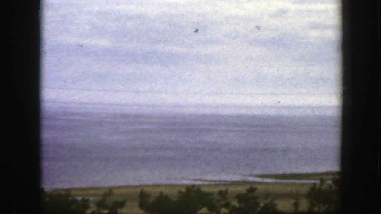 Cloudy sky over calm water and a low shoreline, framed by dark vertical borders.