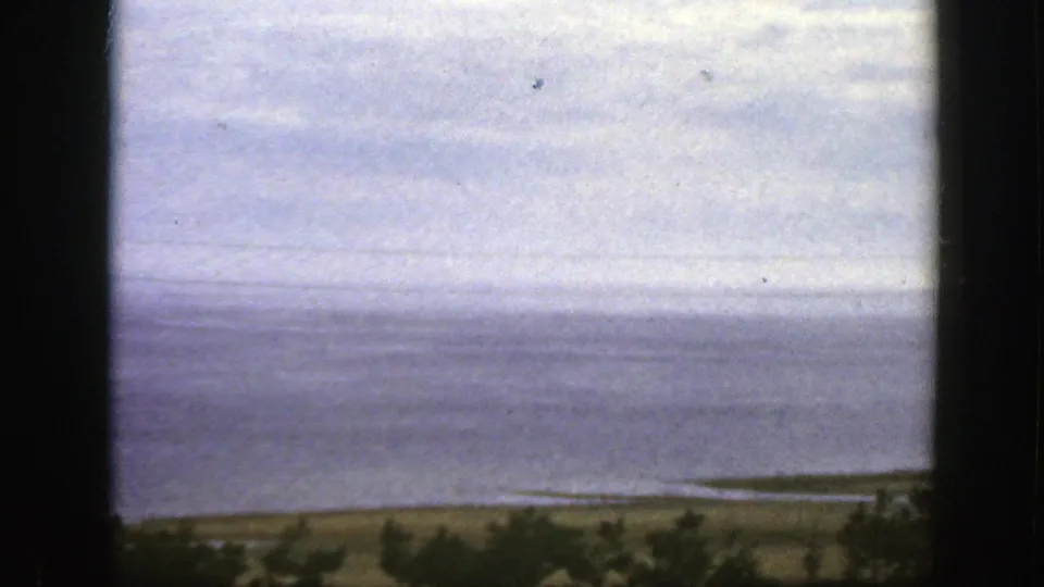 1950 8mm Montreal-area home-movie view of calm water, cloudy sky, and distant shoreline seen through dark vertical framing.