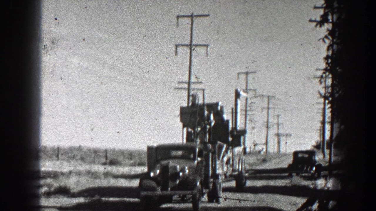 Vehicle or tractor-like hauler towing equipment on a rural road with utility poles behind it.