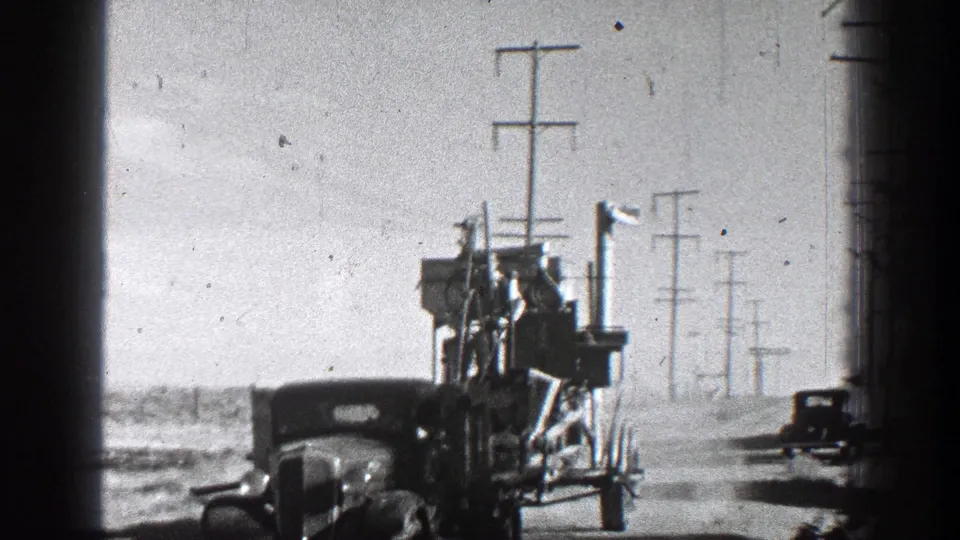 1936 California home-movie frame with a hauler and large towed equipment on a rural road, with a second vehicle and utility poles receding into the background.