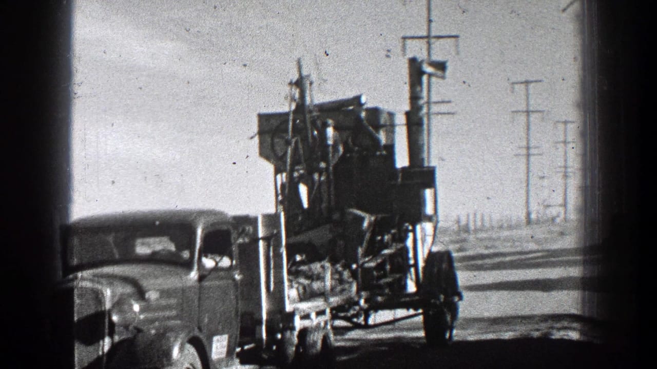 Vintage truck towing farm machinery along a rural road with utility poles.