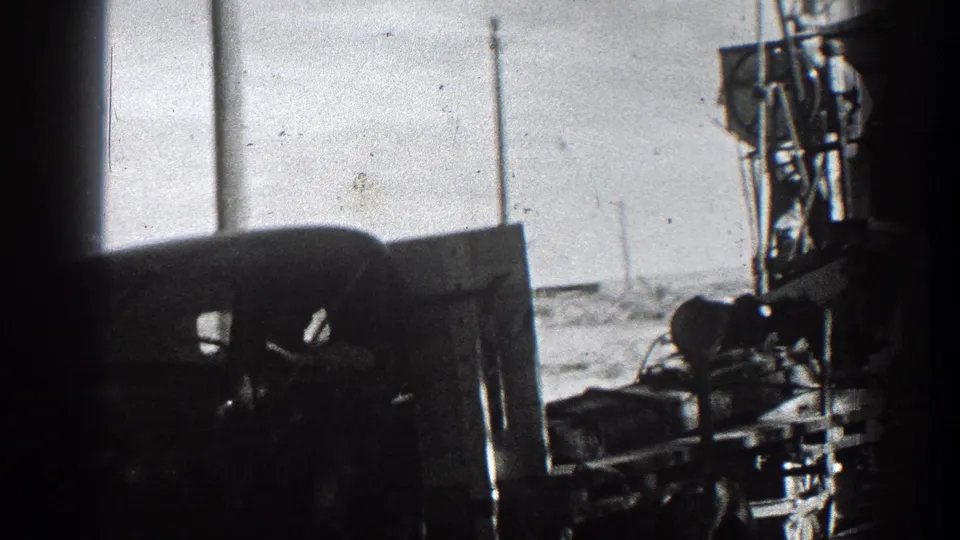 Side view from 1936 California footage showing the truck and towed farm machinery moving past a roadside utility line.