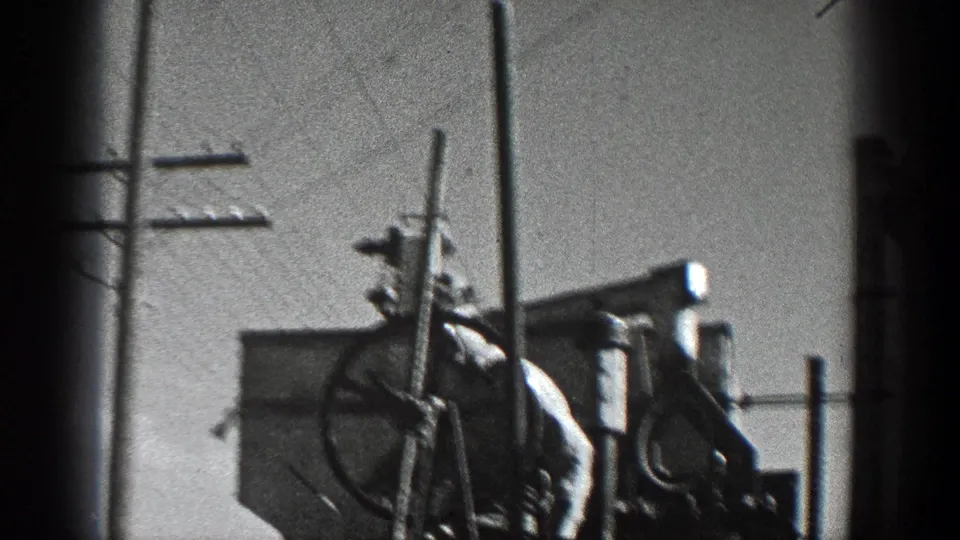 1936 California home-movie frame showing utility pole equipment, crossarms, wires, and a round metal component against open sky.