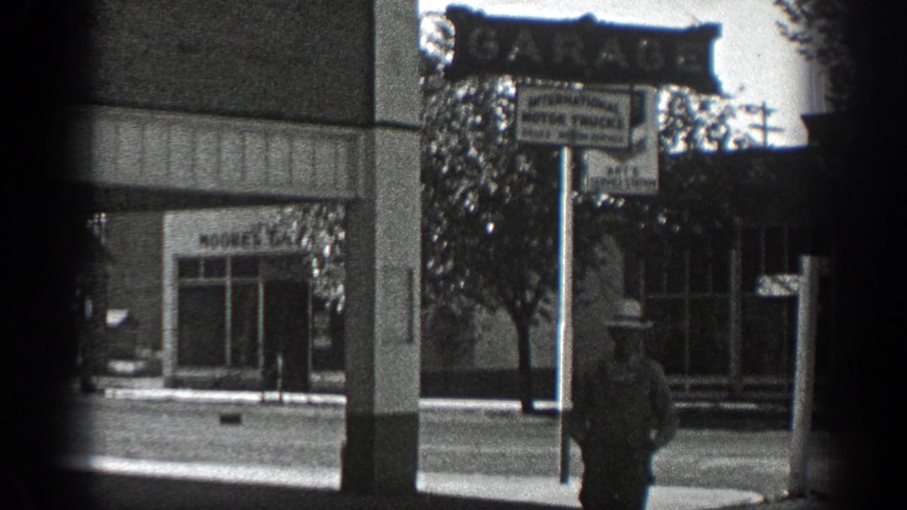 Man in a wide-brimmed hat walking near a garage sign on a downtown street.