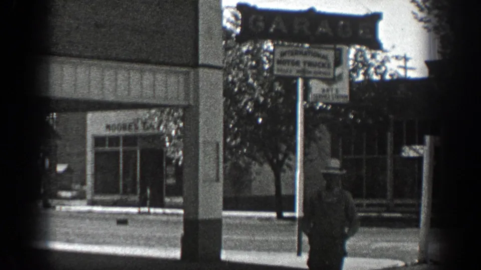 1936 California street view with a pedestrian, garage signage, storefronts, and a partially visible business block across the road.