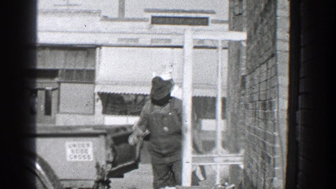 Man in overalls and hat standing beside the open rear of a truck near a storefront.