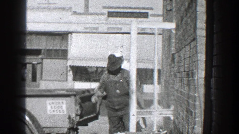 1936 California street scene with a man in overalls and a brimmed hat working at the rear of a truck near a storefront and awning.