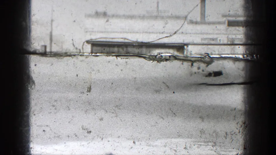 A transitional 8mm frame shows a pale storefront view with heavy film wear and only partial street details visible.