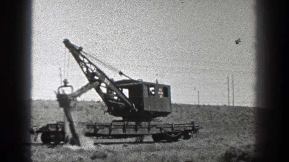 1936 California frame showing the crane boom angled over a dirt worksite as the bucket hangs low near the ground.