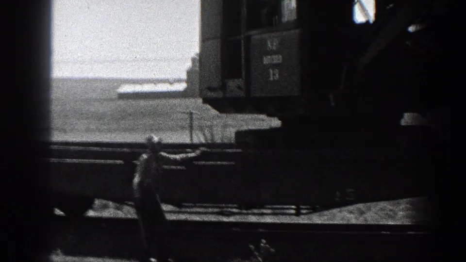 High-contrast 8mm frame of the machine's side and cab against a bright rural California field background.