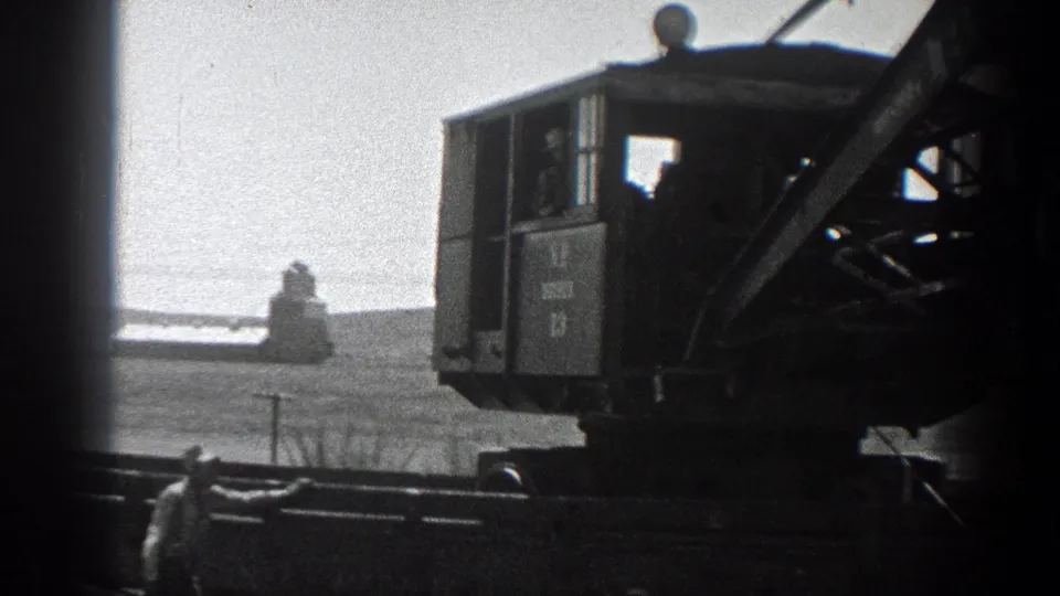 1936 California frame showing a worker near foreground rails or pipes beside the cab of a tracked field machine.