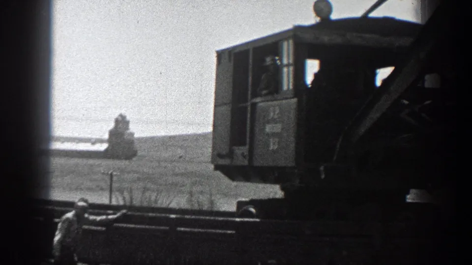 Final 8mm frame with a worker by foreground lines and a tracked machine cab in a rural 1936 California setting.