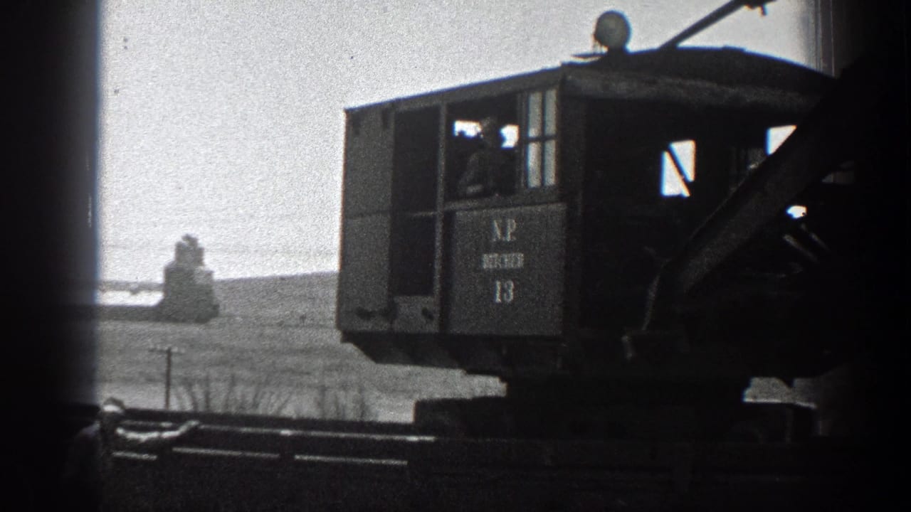 1936 California 8mm frame showing a marked steam crane cab, boom, and rail equipment against dry hills.