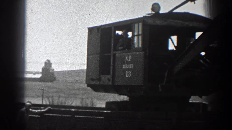 1936 California 8mm frame showing a marked steam crane cab, boom, and rail equipment against dry hills.