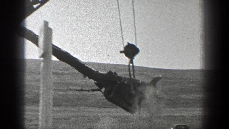 1936 California 8mm frame showing a crane bucket and boom working near a rail line in a dry landscape.