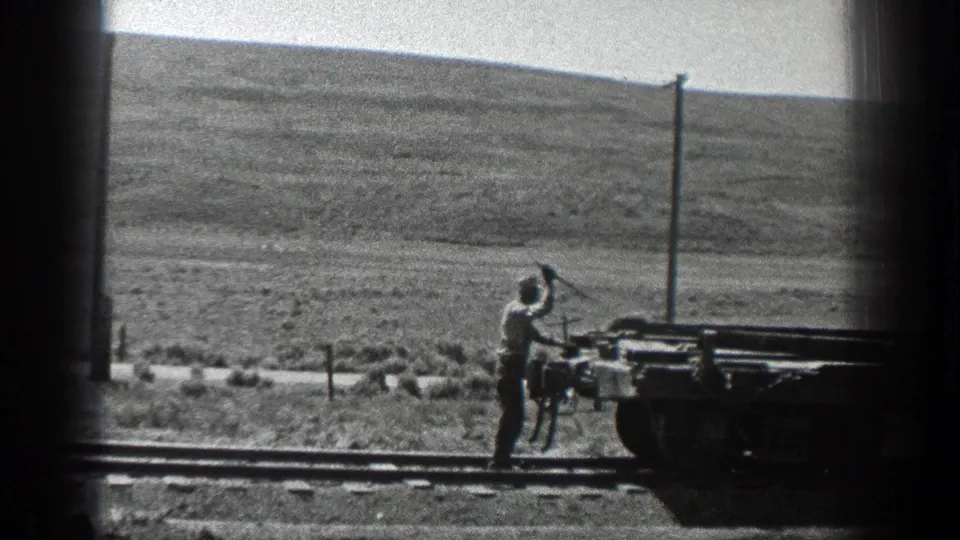 1936 California 8mm frame showing a worker beside tracks and rail equipment in a sparse construction landscape.