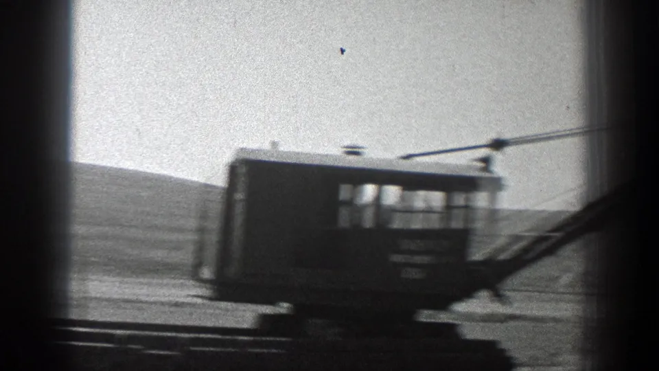 1936 California 8mm frame showing a crane cab in motion with boom cables against a bright open landscape.