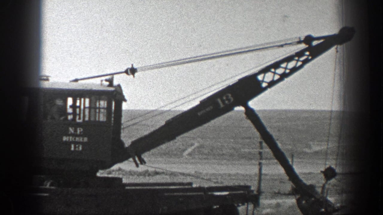 Rail-mounted crane with lattice boom beside open hills and utility lines.