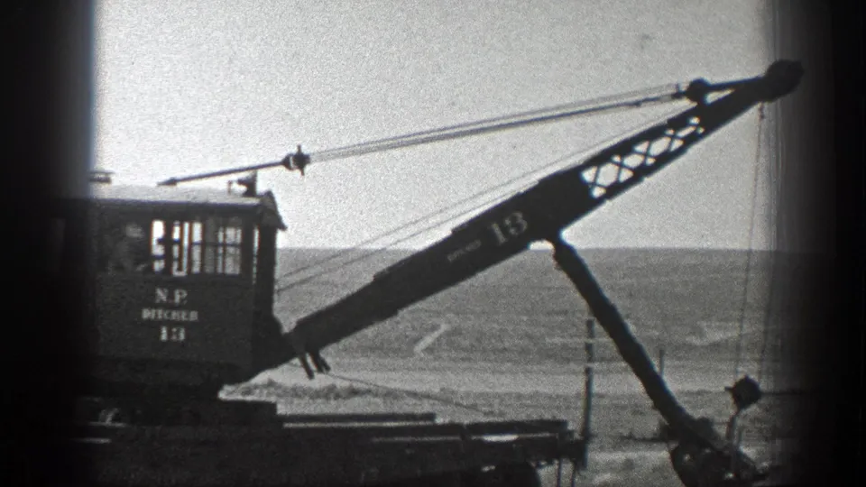 1936 California 8mm frame showing a rail crane marked with numbers, its boom extended across a rural trackside landscape.