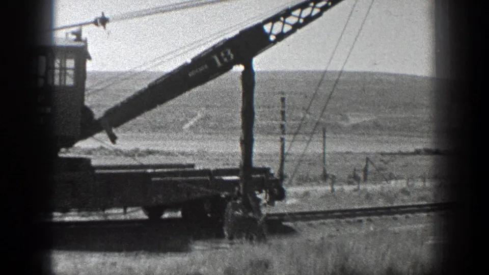 The rail-mounted crane appears in profile, with its boom angled across the frame and dry California hills beyond.