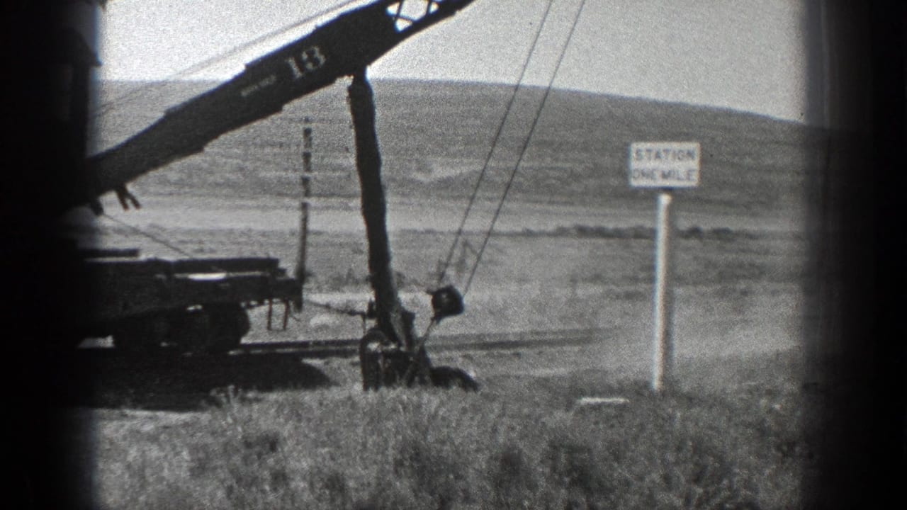 1936 California 8mm frame showing a rail-mounted crane numbered 13 moving earth beside track, utility poles, and a Station One Mile sign.