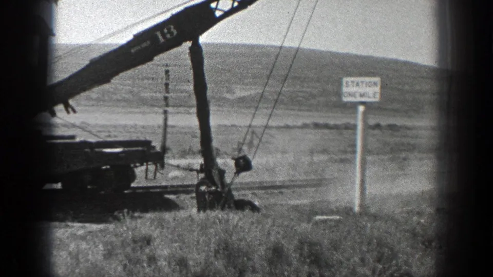 1936 California 8mm frame showing a rail-mounted crane numbered 13 moving earth beside track, utility poles, and a Station One Mile sign.