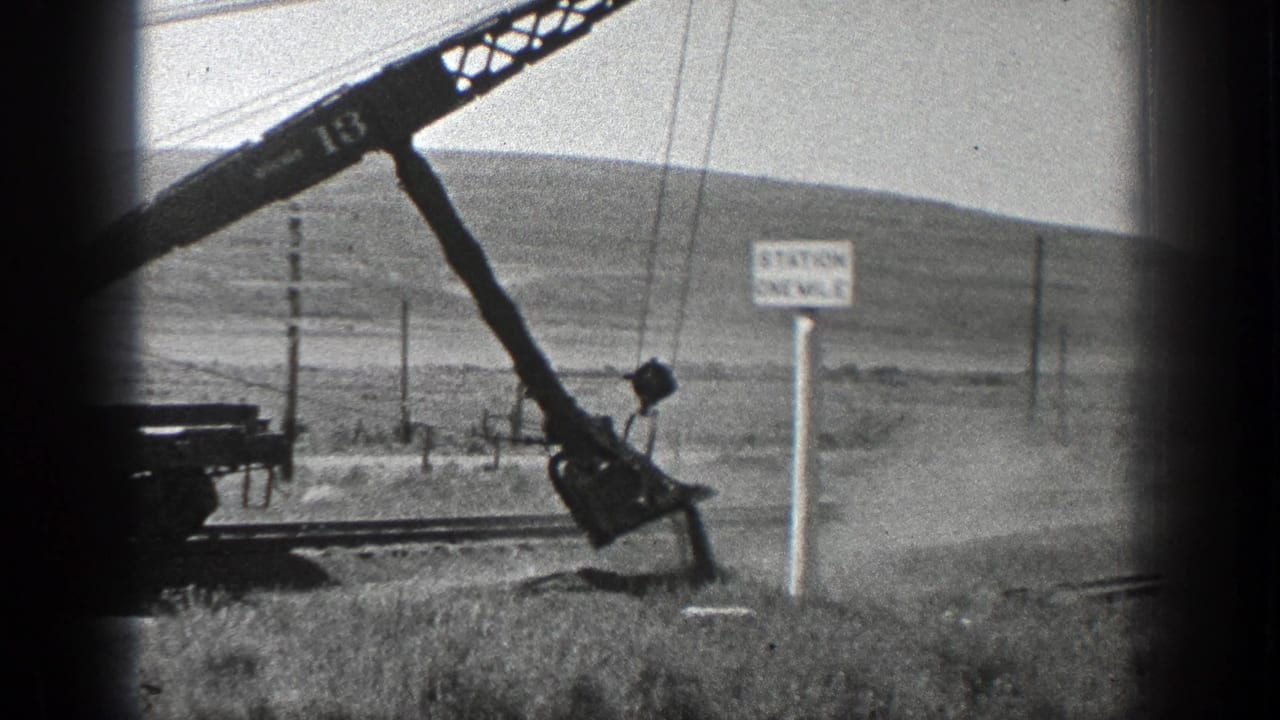 Crane bucket scrapes dusty ground beside track and a Station One Mile sign.