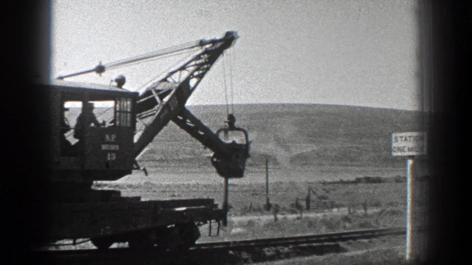 1936 California frame showing the crane cab, silhouetted operator, boom, bucket, rails, and rural station-distance sign.