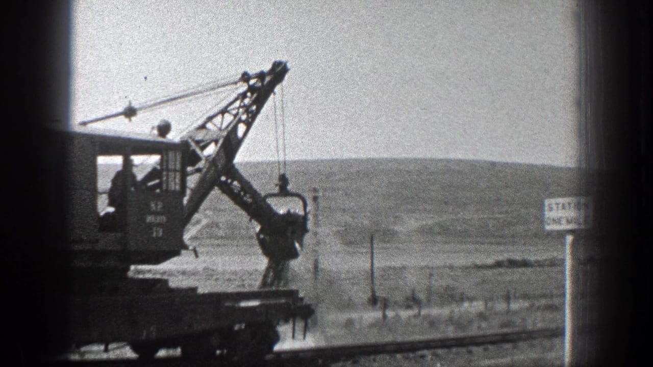 Crane-mounted rail equipment beside tracks in open countryside.