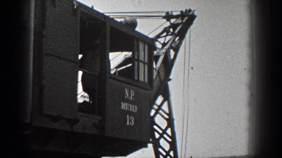 Large industrial crane cab in 1936 California footage, with a person inside, boom structure, cables, and painted equipment markings.